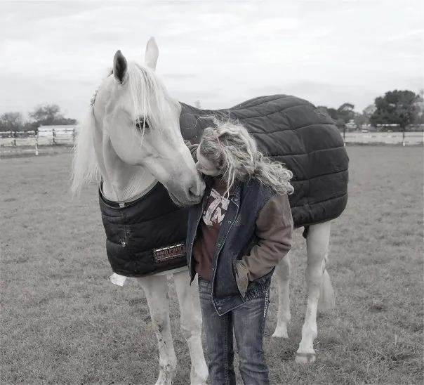 A girl is petting a horse in a blanket.