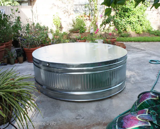 A metal watering can sitting on a concrete patio.