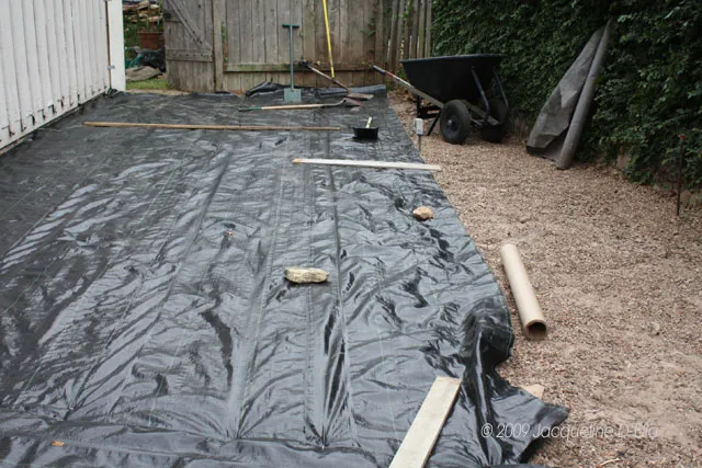 A black tarp is laid out in a backyard.