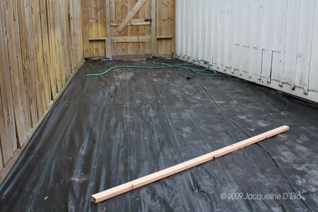 A black tarp on the ground next to a wooden fence.