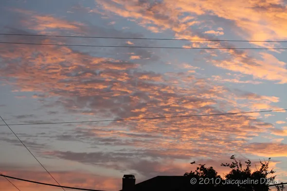 A sunset over a house with power lines in the background.