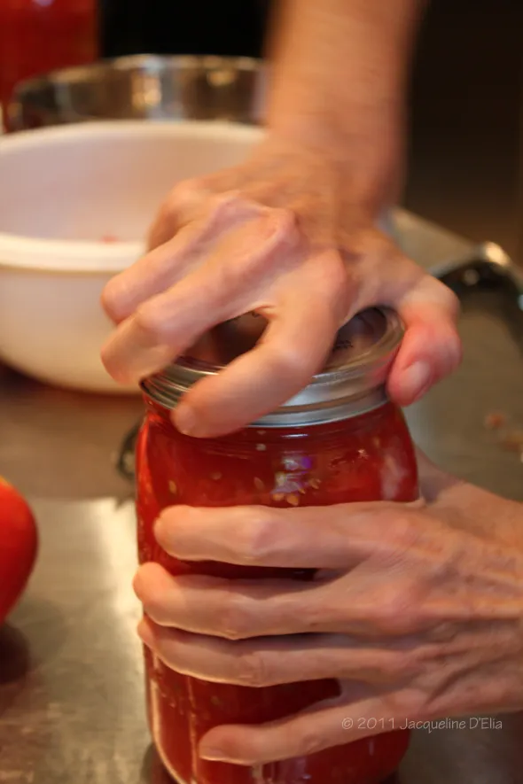 A person is canning a jar of tomato sauce.