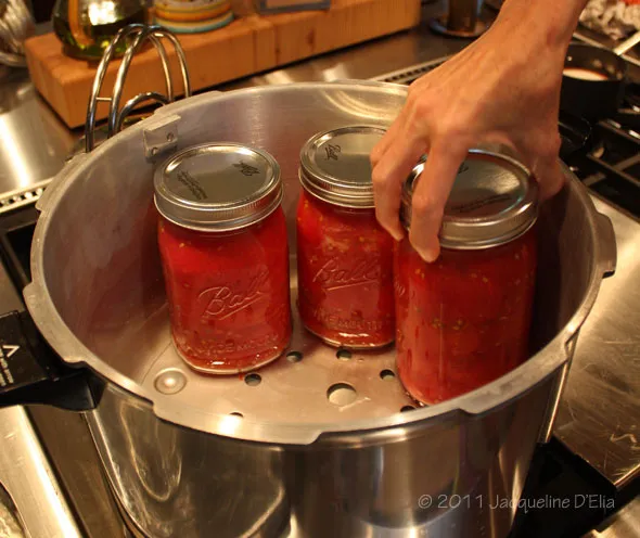 Three jars of canned tomato sauce simmering on a stove.
