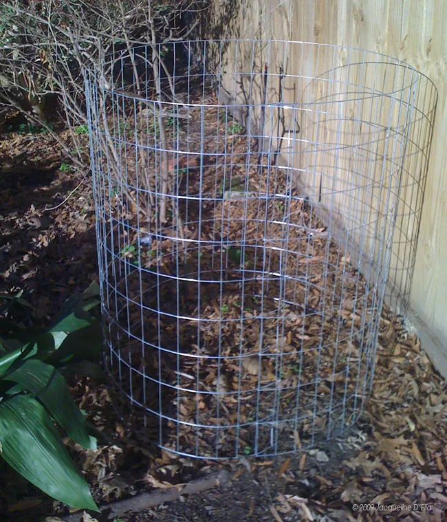 A compost bin sitting on the ground next to a fence.
