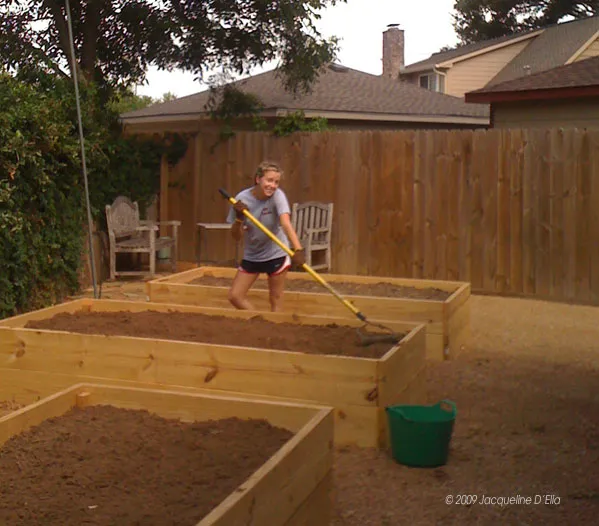 A woman is digging in a raised garden bed.