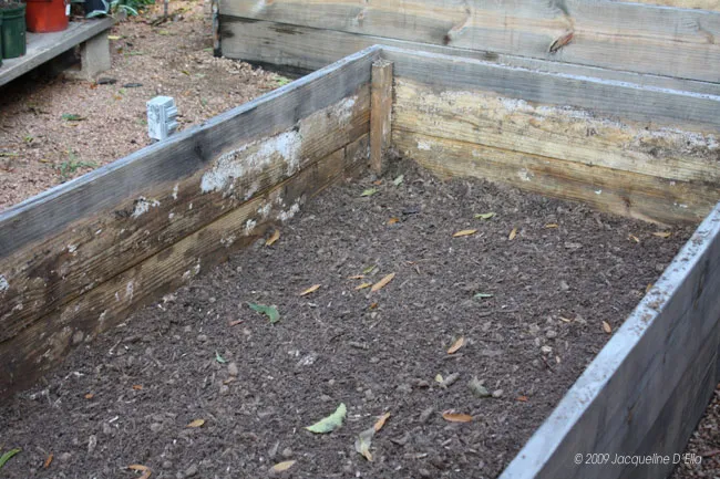 A wooden raised garden bed filled with dirt.