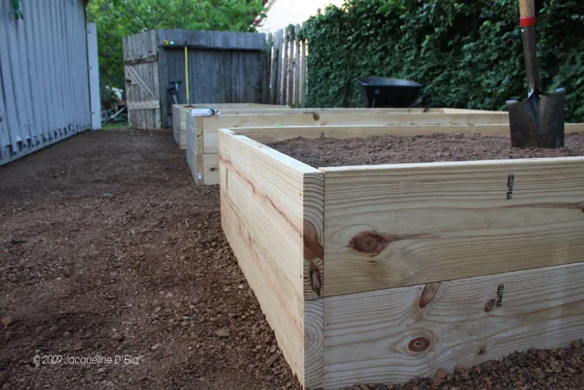 A raised garden bed with a shovel in the dirt.