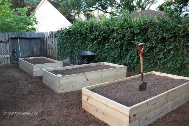 Three raised garden beds in a backyard with a shovel.