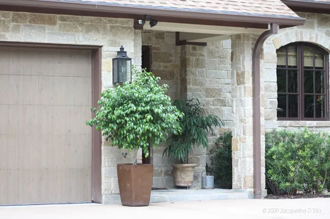 A house with a potted plant in front of the garage door and a kitchen garden.