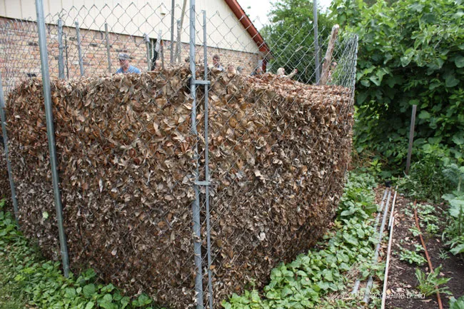 A large pile of leaves on a fence next to a garden.