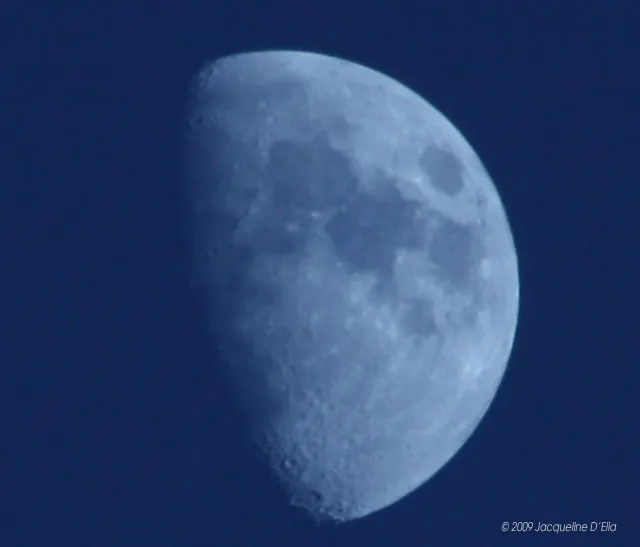 The moon is seen through a clear blue sky.