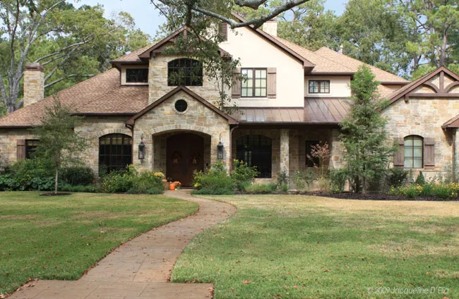 A large stone house with a walkway and a kitchen garden in the front yard.